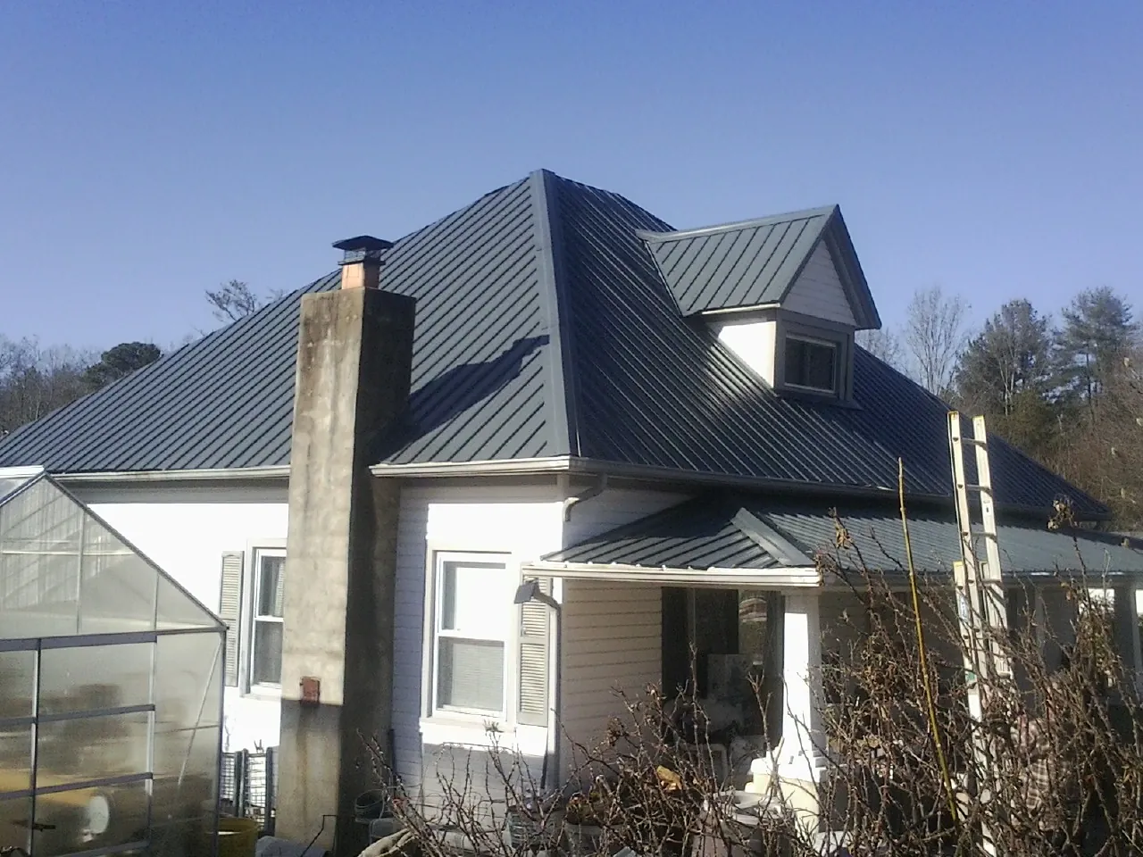 Dark blue standing seam metal roof on a white farmhouse with dormer — Slate & Tile Roof Repair by Roofing Brothers in Blomkest