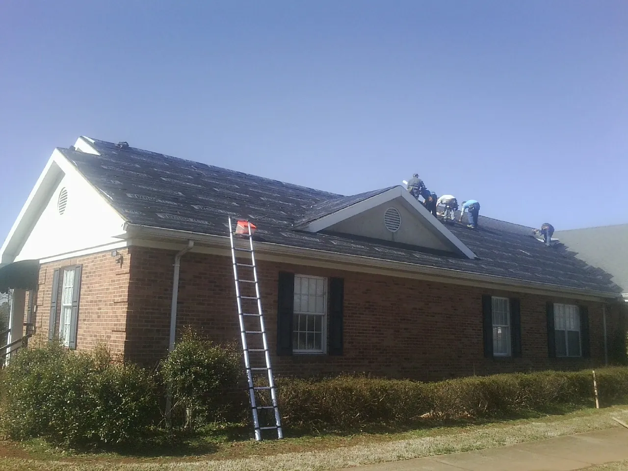 Crew tearing shingles off a brick ranch roof with a ladder set — Metal Roof Repair work by our crew in Blomkest