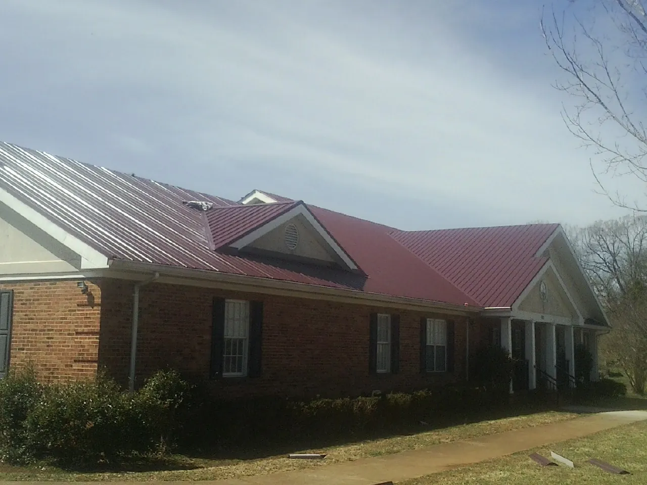 Red metal roof with gabled entries on a long brick building, from a Hail Damage Roof Repair job in Blomkest