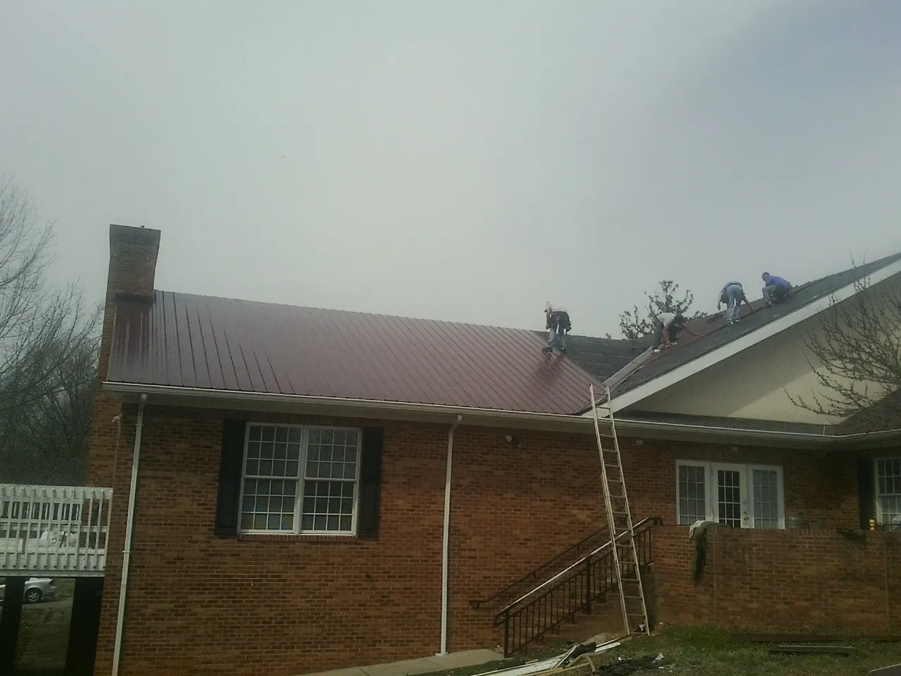 Crew setting red metal roofing panels on a brick home in Blomkest