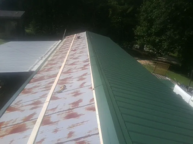 Old rusted panels beside newly installed green metal roofing — Wind Damage Roof Repair by Roofing Brothers in Blomkest