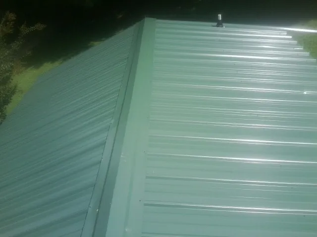 New green metal panels meeting at the ridge of a roof — Flat Roof Repair work by our crew in Blomkest