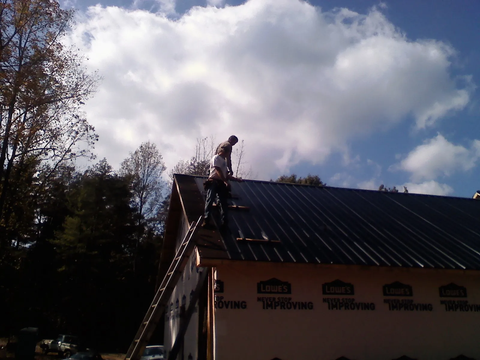 Roofer fastening dark metal panels high against a cloudy sky, from a Roof Inspection job in Blomkest