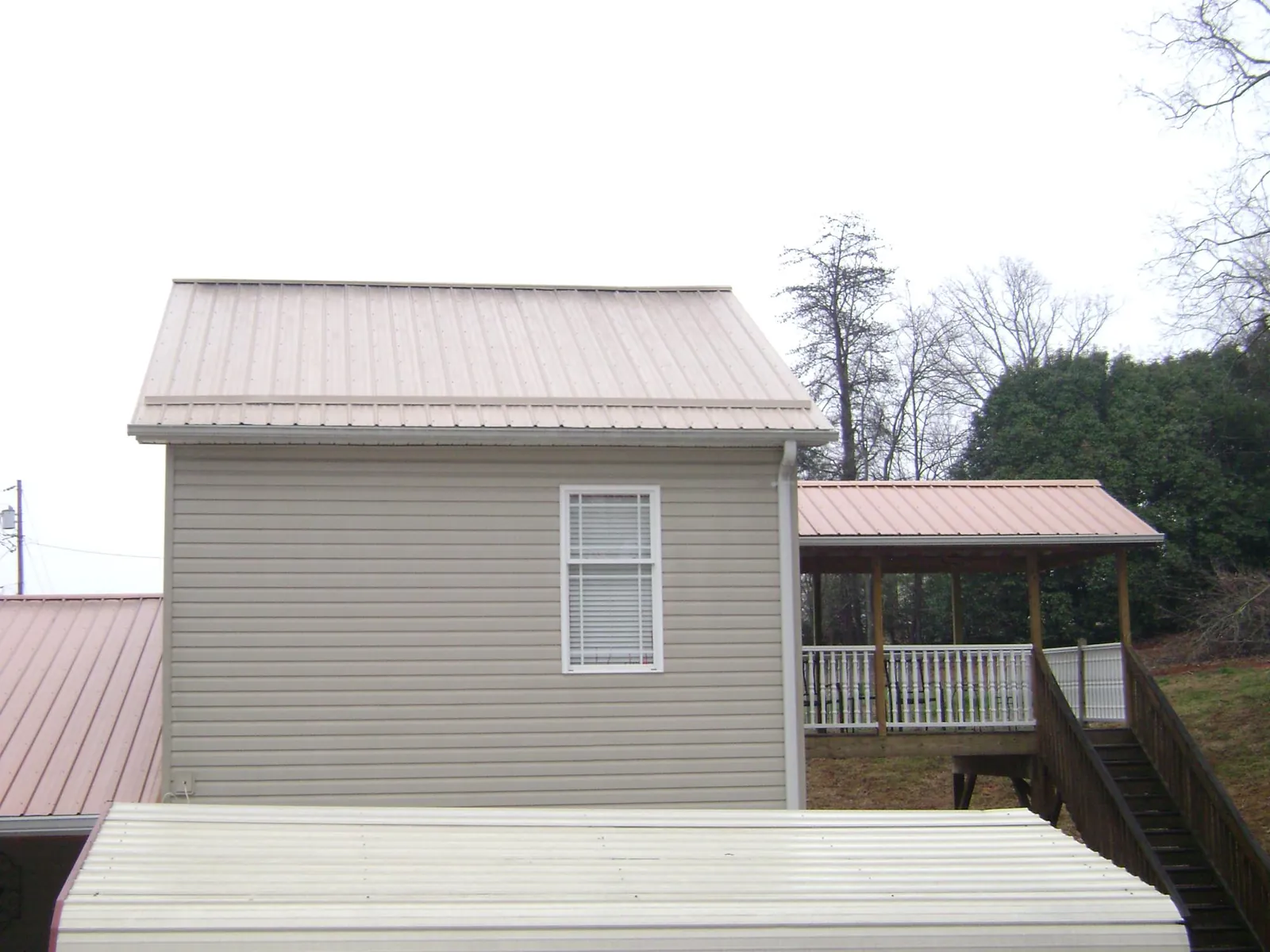 Tan metal roofs on a two story addition and attached porch, from a Roof Replacement job in Blomkest